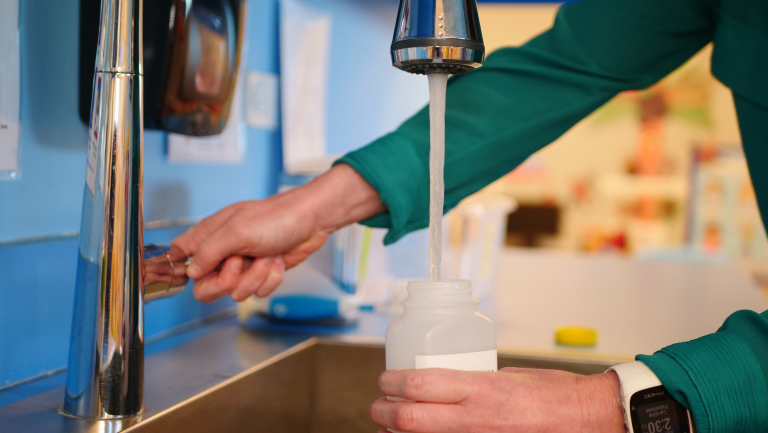 child care provider collecting water sample at sink faucet